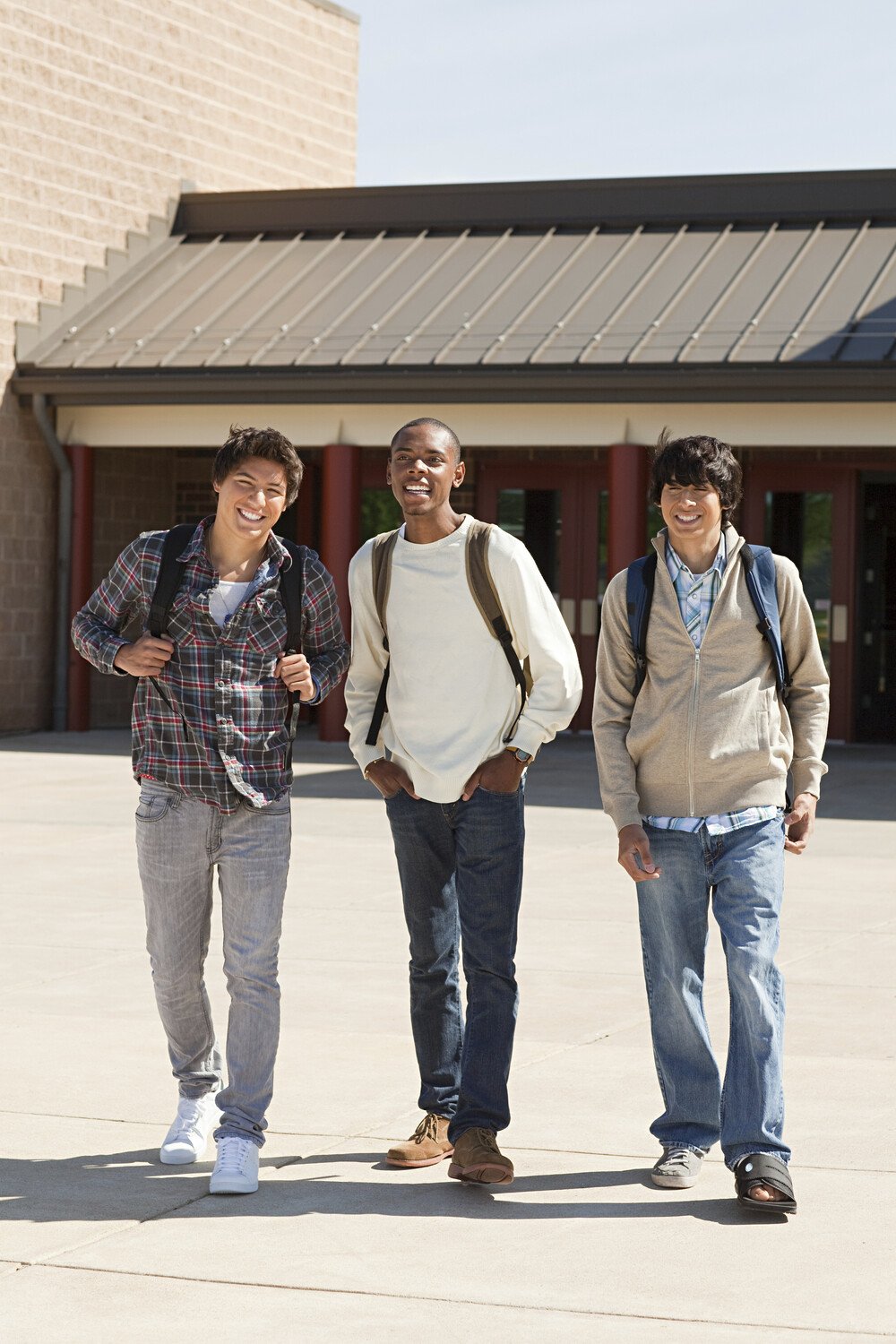 Three friends laughing and walking together outside of a school building.